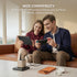 Two people sitting on a couch using electronic devices with a charging station in front of them.