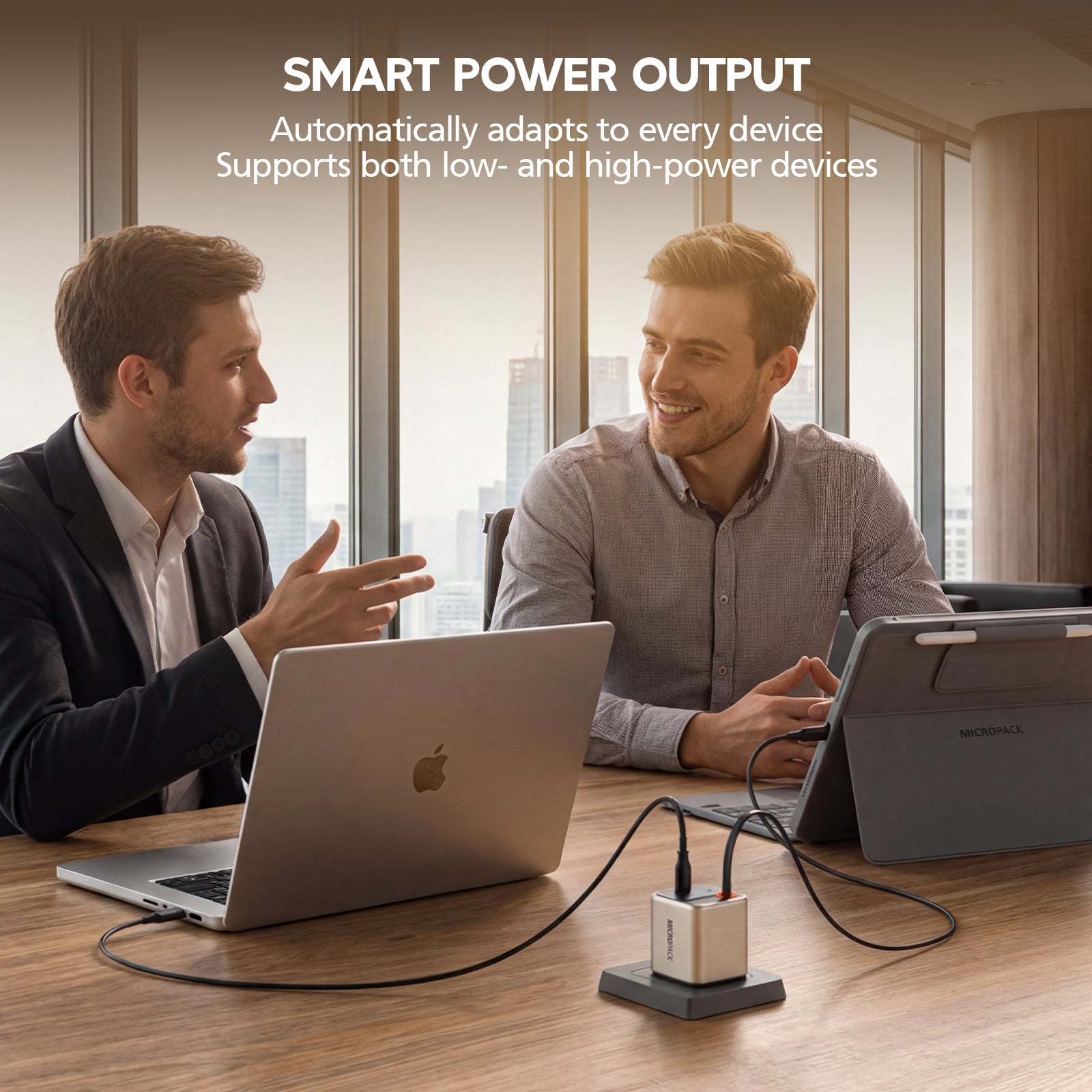 Two men sitting at a table with laptops, using a smart power output device.
