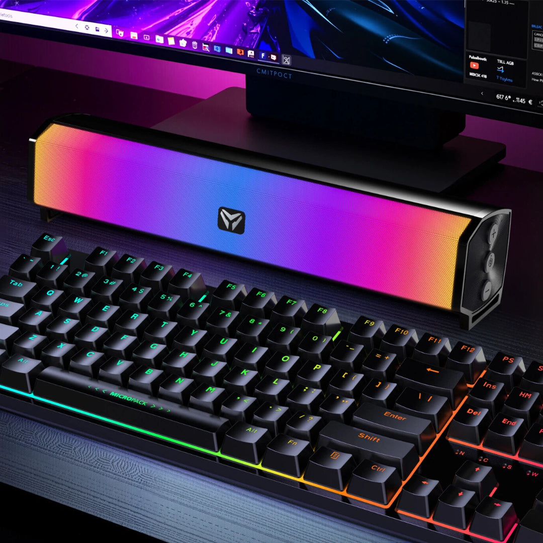 Gaming keyboard and RGB light bar on a desk with computer monitor in the background