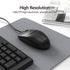 Black computer mouse on a gray mouse pad with keyboard and newspaper in the background, featuring text about high resolution.