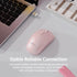 A light pink wireless computer mouse on a light gray desk surface, styled with a laptop corner, a USB receiver, a book, and promotional text reading 'Stable Reliable Connection' and 'Advanced 2.4GHz wireless technology provide strong stable and reliable connection up to 10 meters, with virtually no delays or dropouts.