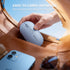 Hand placing a wireless mouse into a brown leather bag with a phone and sunglasses nearby.