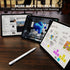 Three tablets on a wooden surface displaying different apps with a pen in front.