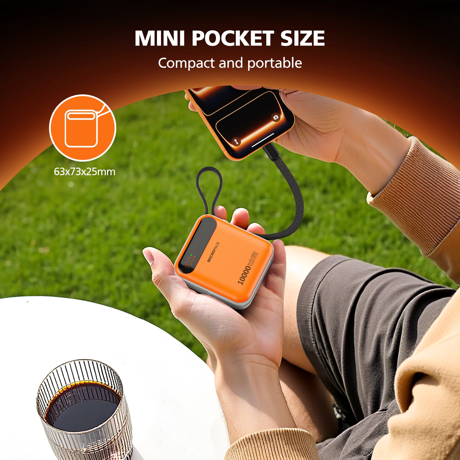Person holding a small orange power bank with grass and coffee cup in the background